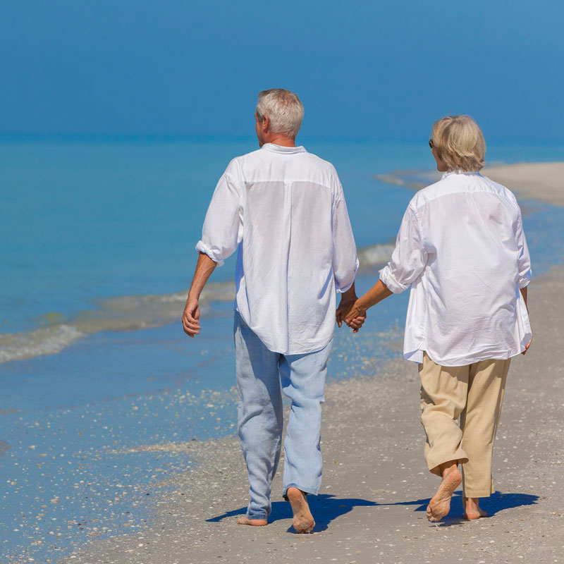 Ein älteres Paar geht händchenhaltend am Strand spazieren